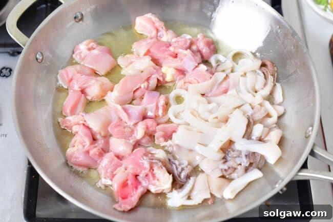 A Family's Cherished Paella 5 Diced chicken and calamari are being seared in a wide, shallow paella pan with olive oil over medium-high heat.