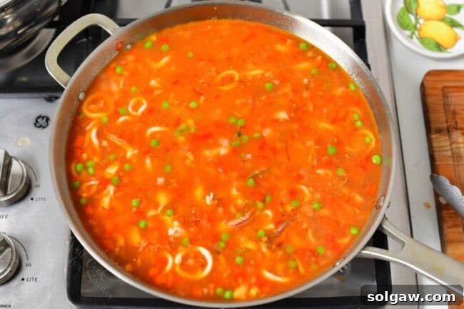 A Family's Cherished Paella 8 A paella dish is cooking uncovered on a stovetop, with rice and vegetables simmering evenly.