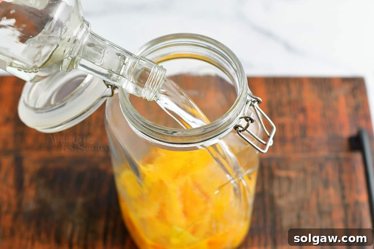 Vodka is being poured into a glass jaw with lemon peels.