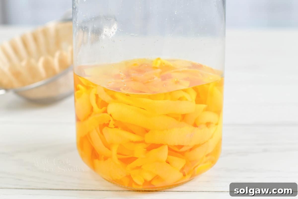 Lemon peels and vodka are combined in a glass jar that's placed on a white countertop.