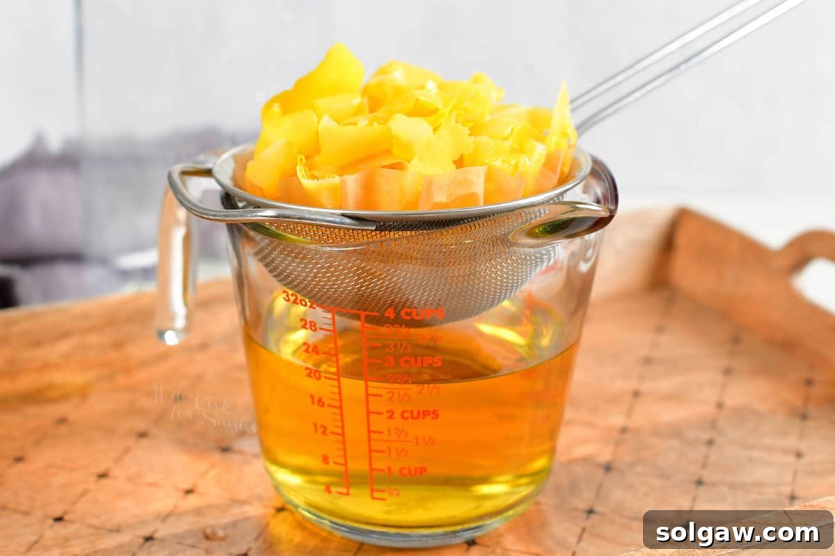 Lemon peels are placed on a mesh strainer above a measuring cup now filled with lemon vodka.