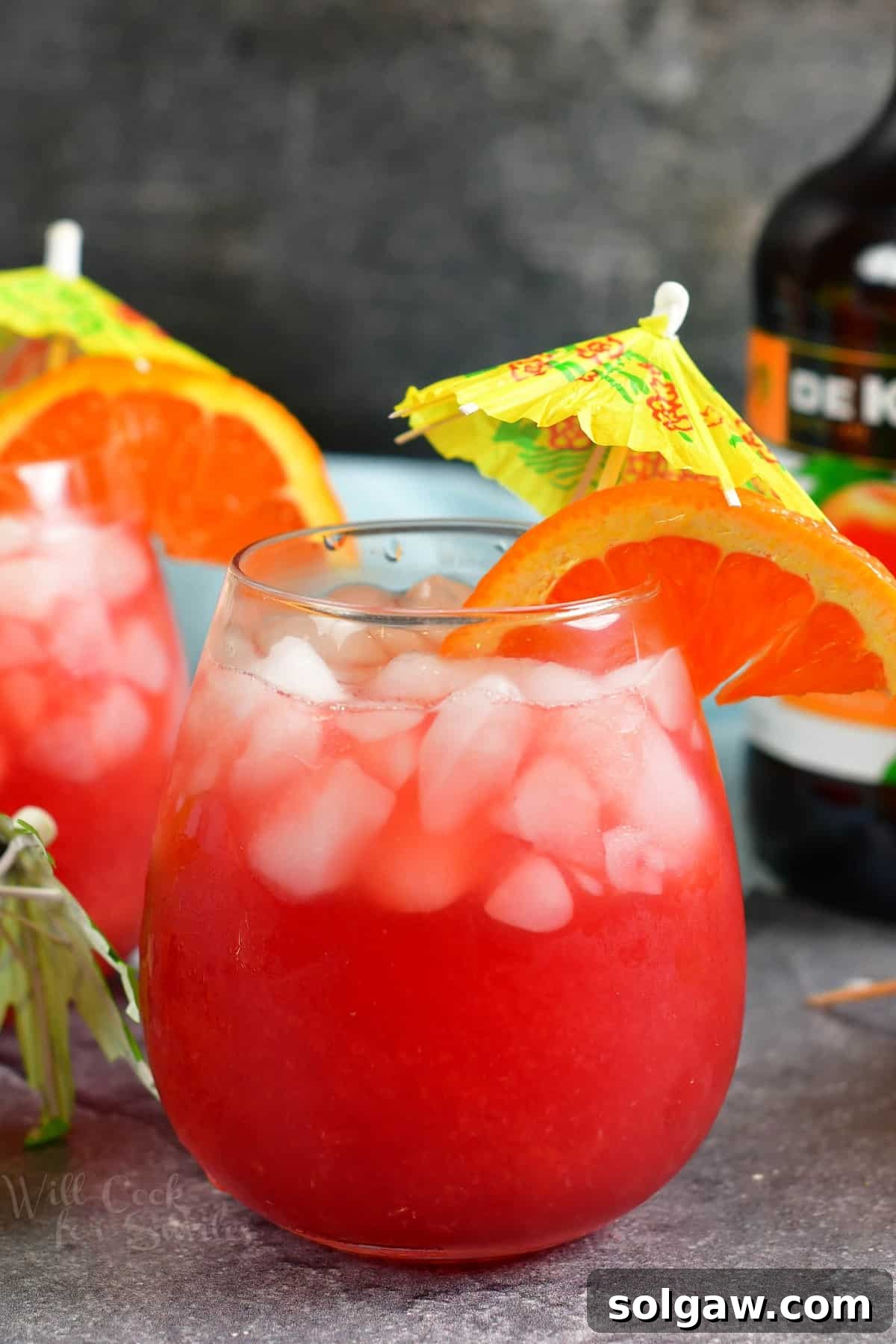 A vibrant red Sex on the Beach cocktail, garnished with a fresh orange wedge and a playful umbrella, sits invitingly.