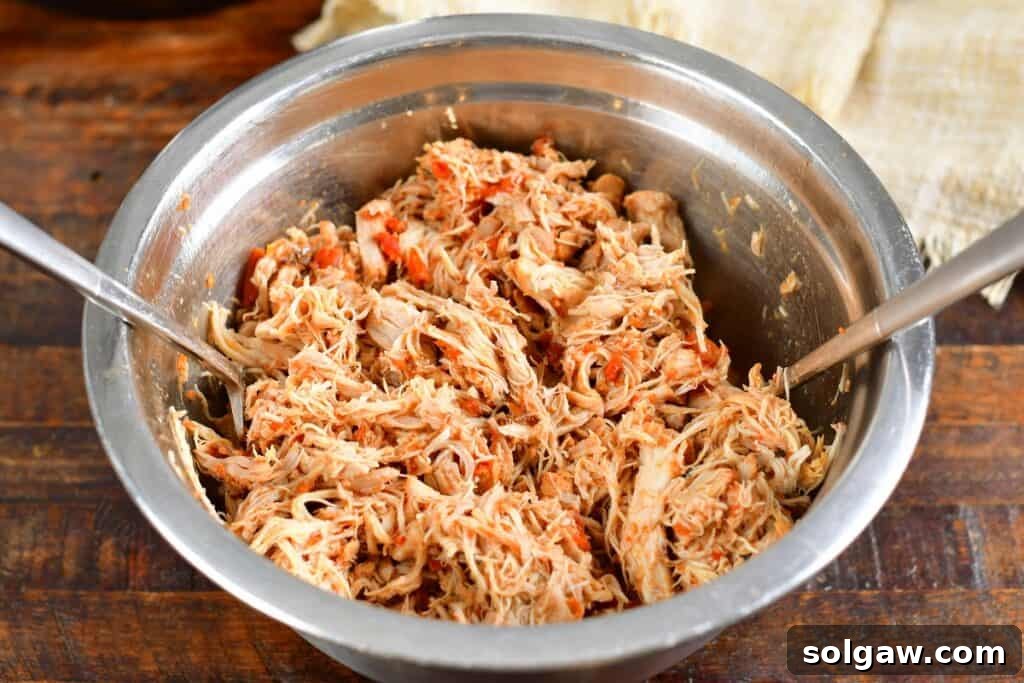 shredding cooked chicken in a metal bowl with two forks