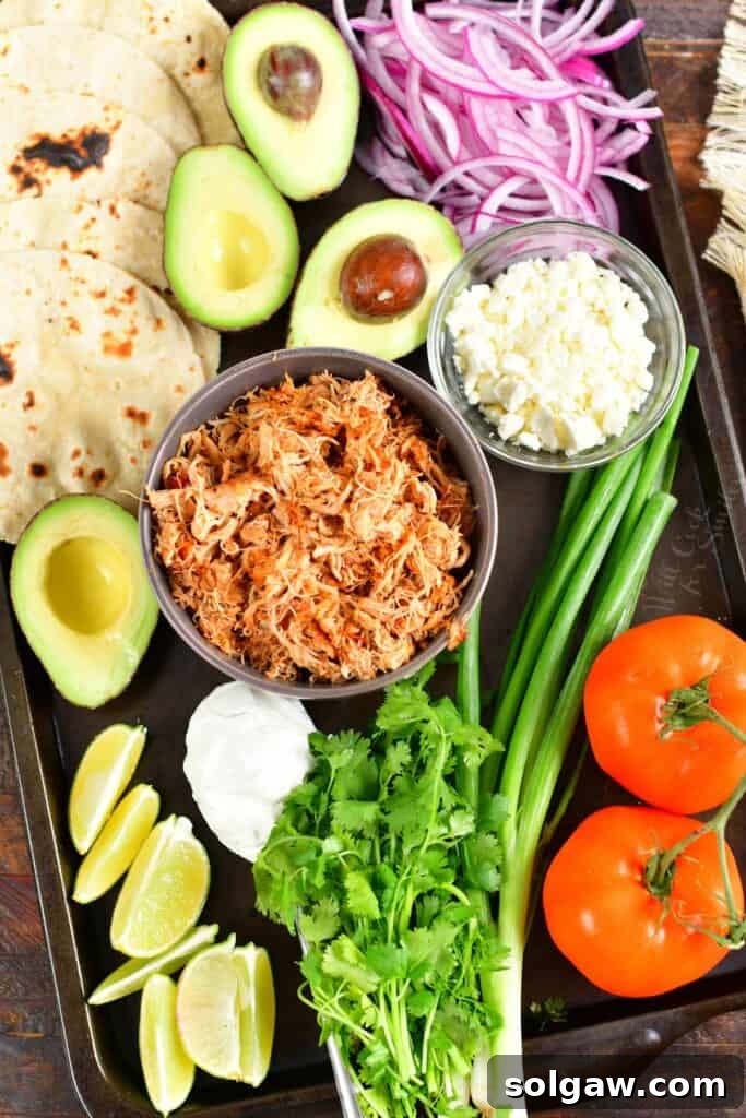 shredded chicken and toppings to make tacos laid out on a sheet pan 