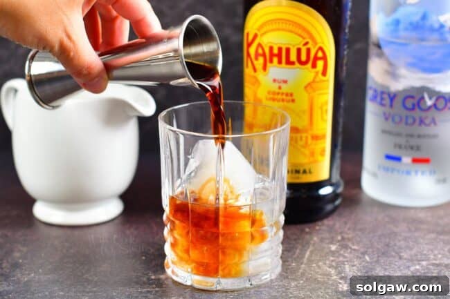 Kahlúa being added to a glass of vodka and ice, creating the base for a White Russian.