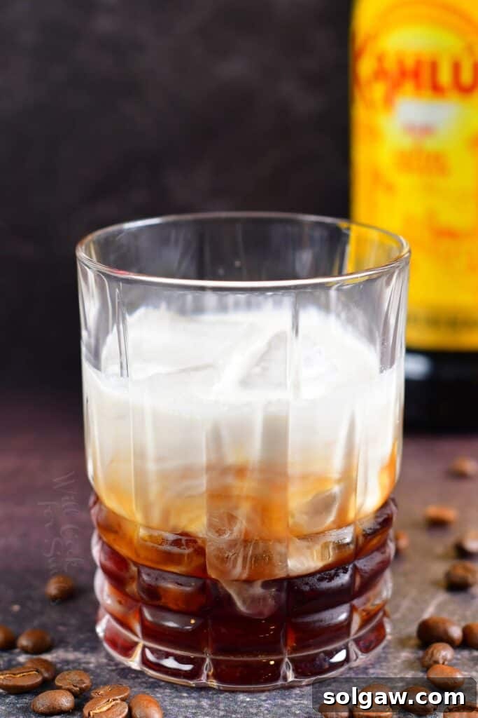 A beautifully layered White Russian cocktail in a glass before mixing, showcasing the distinct layers of cream, Kahlúa, and vodka.