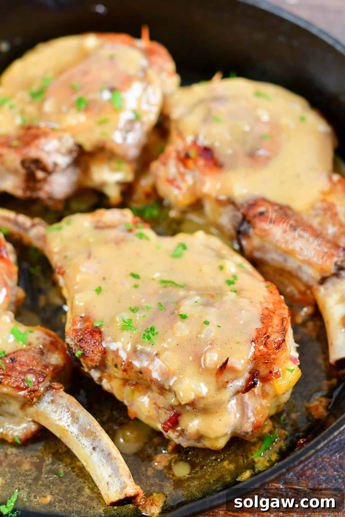 Four golden-brown stuffed pork chops, smothered in a creamy mustard sauce, are beautifully arranged in a large black skillet, ready to be served. The rich colors highlight the dish's deliciousness.