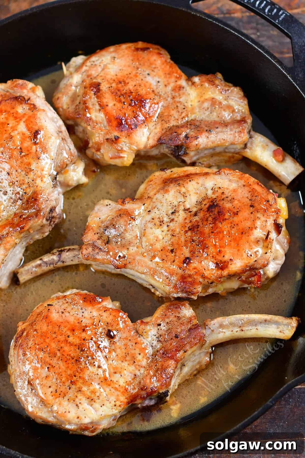 Four perfectly cooked stuffed pork chops, glistening with their golden crust, rest invitingly in a cast-iron skillet after being removed from the oven.