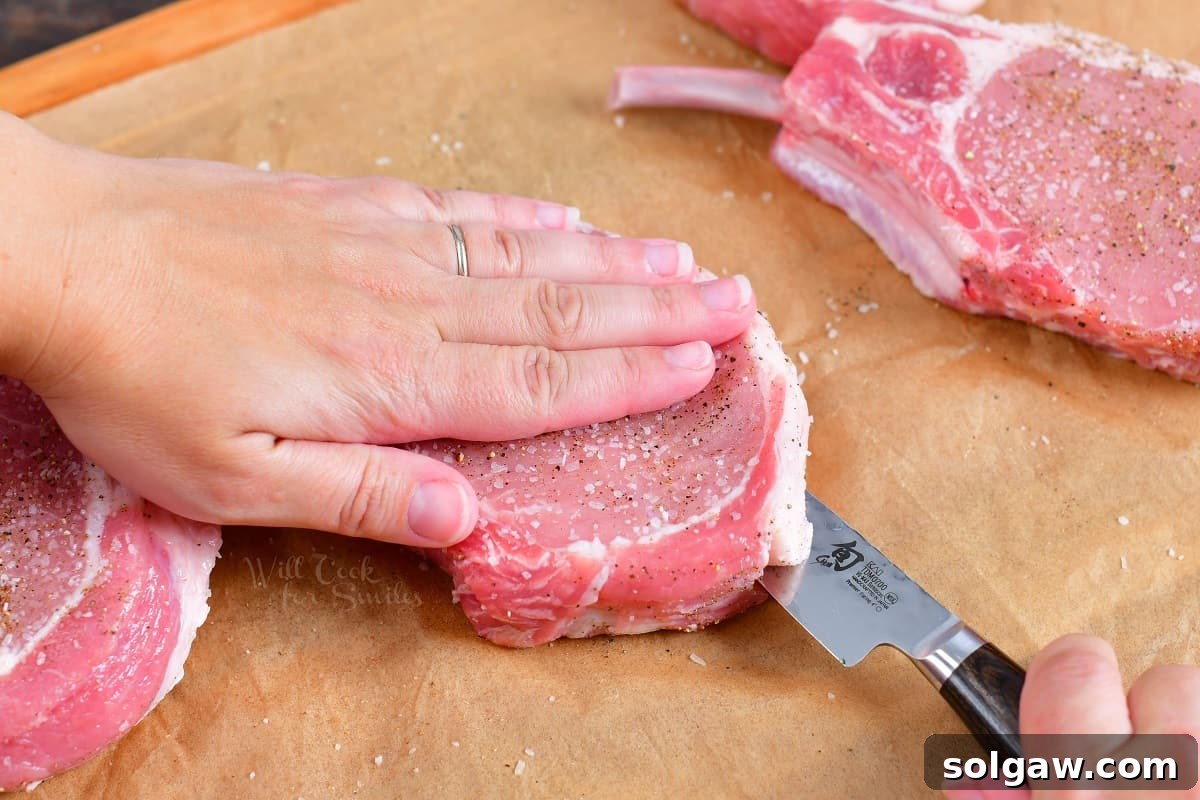 A sharp knife precisely cuts a pocket into the side of a raw pork chop, creating an opening ready for the savory filling.