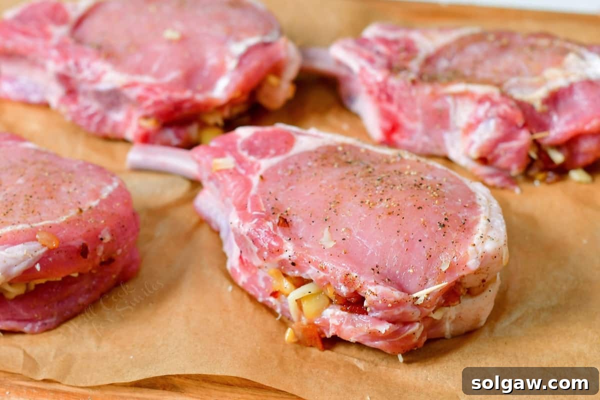 Four raw pork chops, now generously stuffed with the apple and bacon filling, are neatly arranged on a prepared baking sheet, waiting to be seared and roasted.
