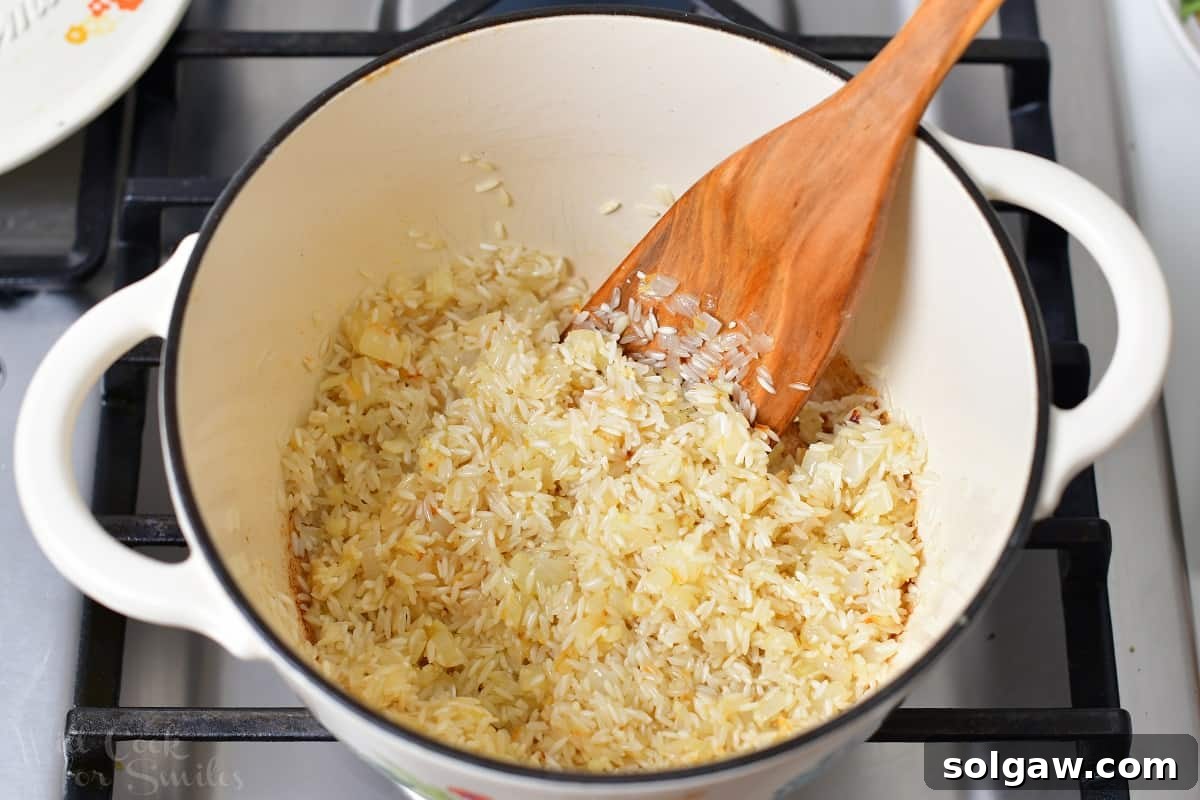 Uncooked long grain white rice being stirred into the aromatic mixture of onions and garlic in a pot, ready for toasting.