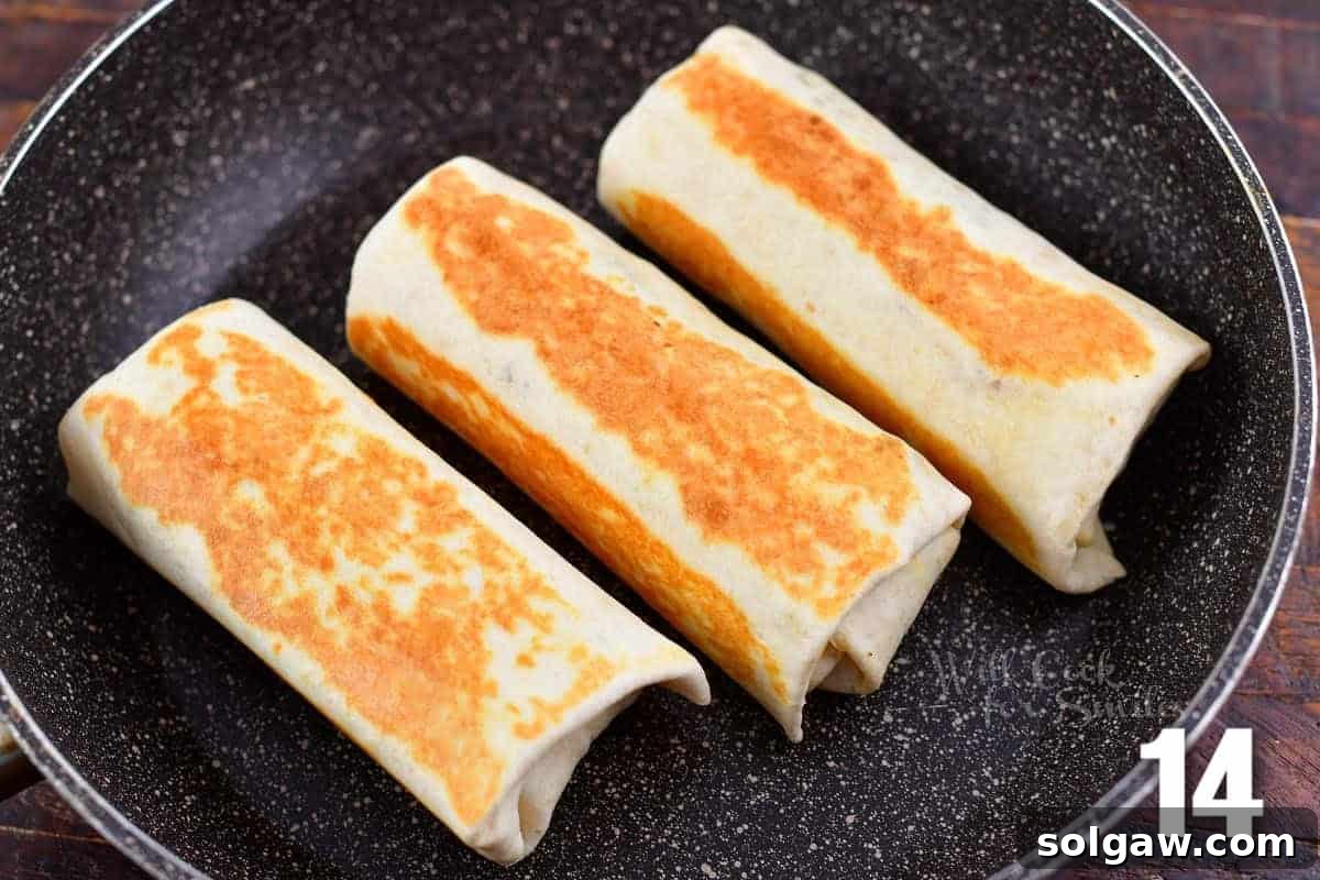 Three perfectly seared breakfast burritos sizzling in a cooking pan, showcasing their golden-brown, crispy exteriors.