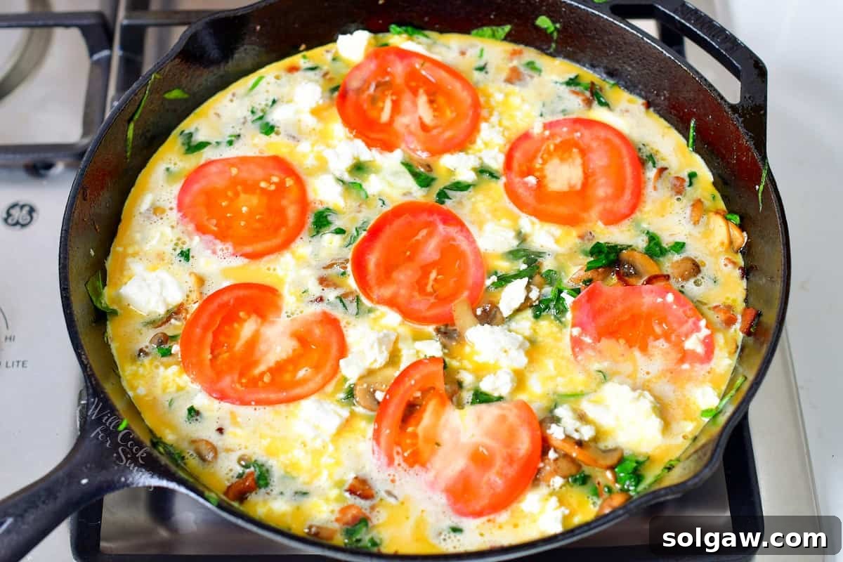 frittata ingredients in a cast iron skillet with tomatoes and feta cheese before baking