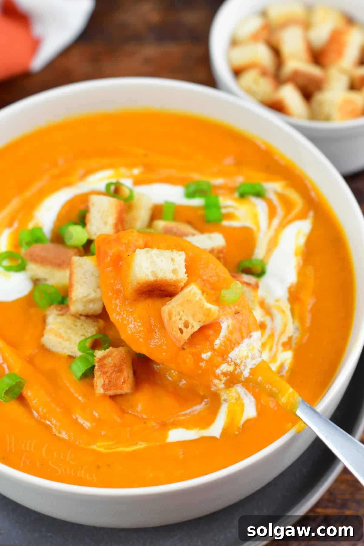 A person spooning out rich sweet potato soup from a bowl, highlighting its smooth and creamy texture.