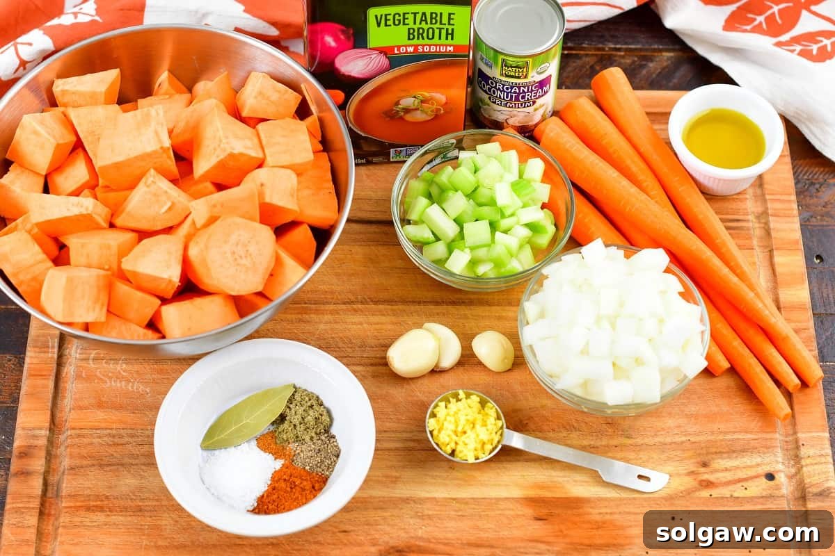 Ingredients for sweet potato soup laid out on a wooden cutting board, including sweet potatoes, carrots, celery, onion, ginger, and spices.