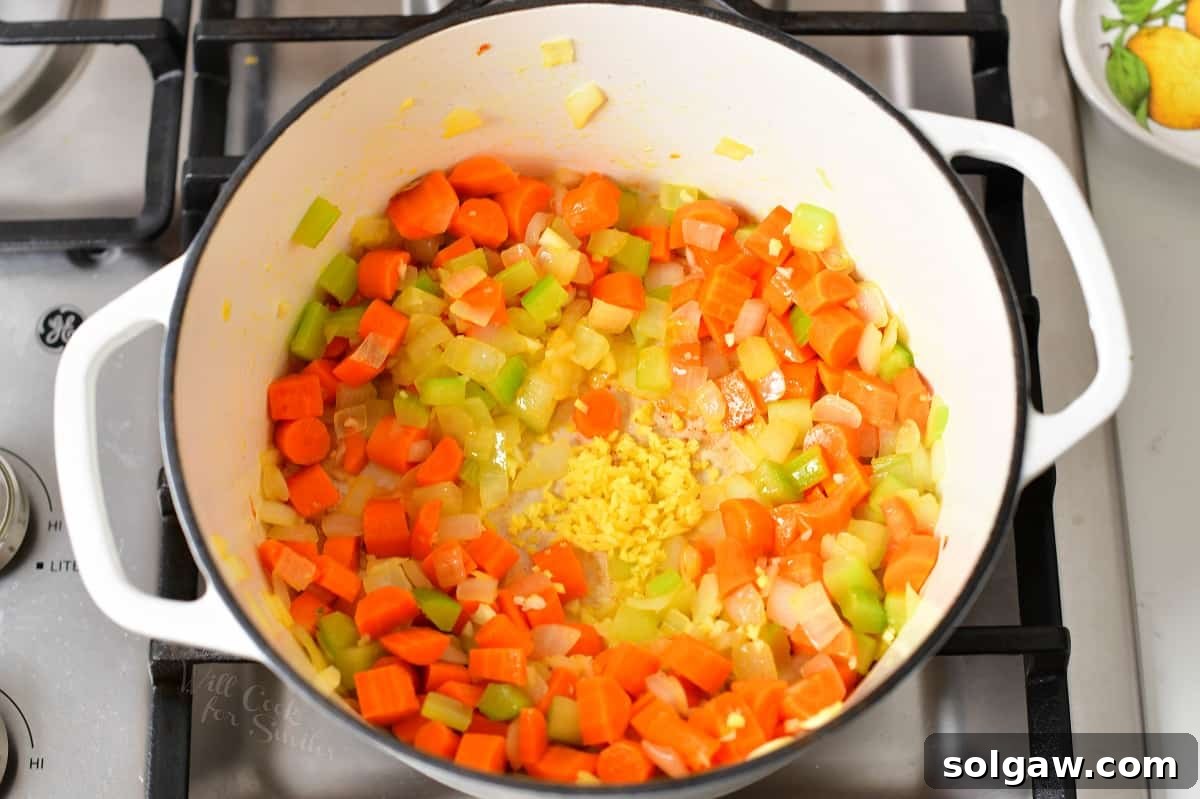 Minced garlic and fresh ginger being added to the center of sautéing vegetables in a pot.