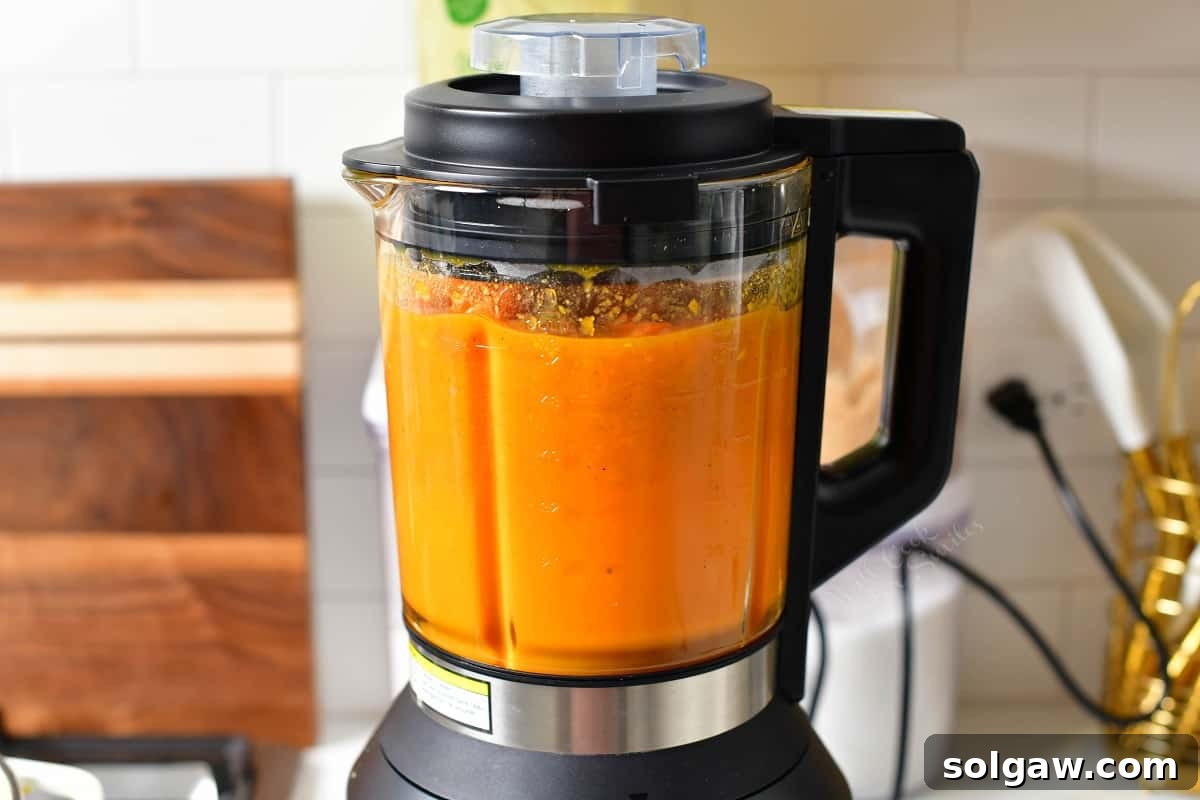 Bright orange sweet potato soup being blended to a silky smooth consistency in a stand blender.