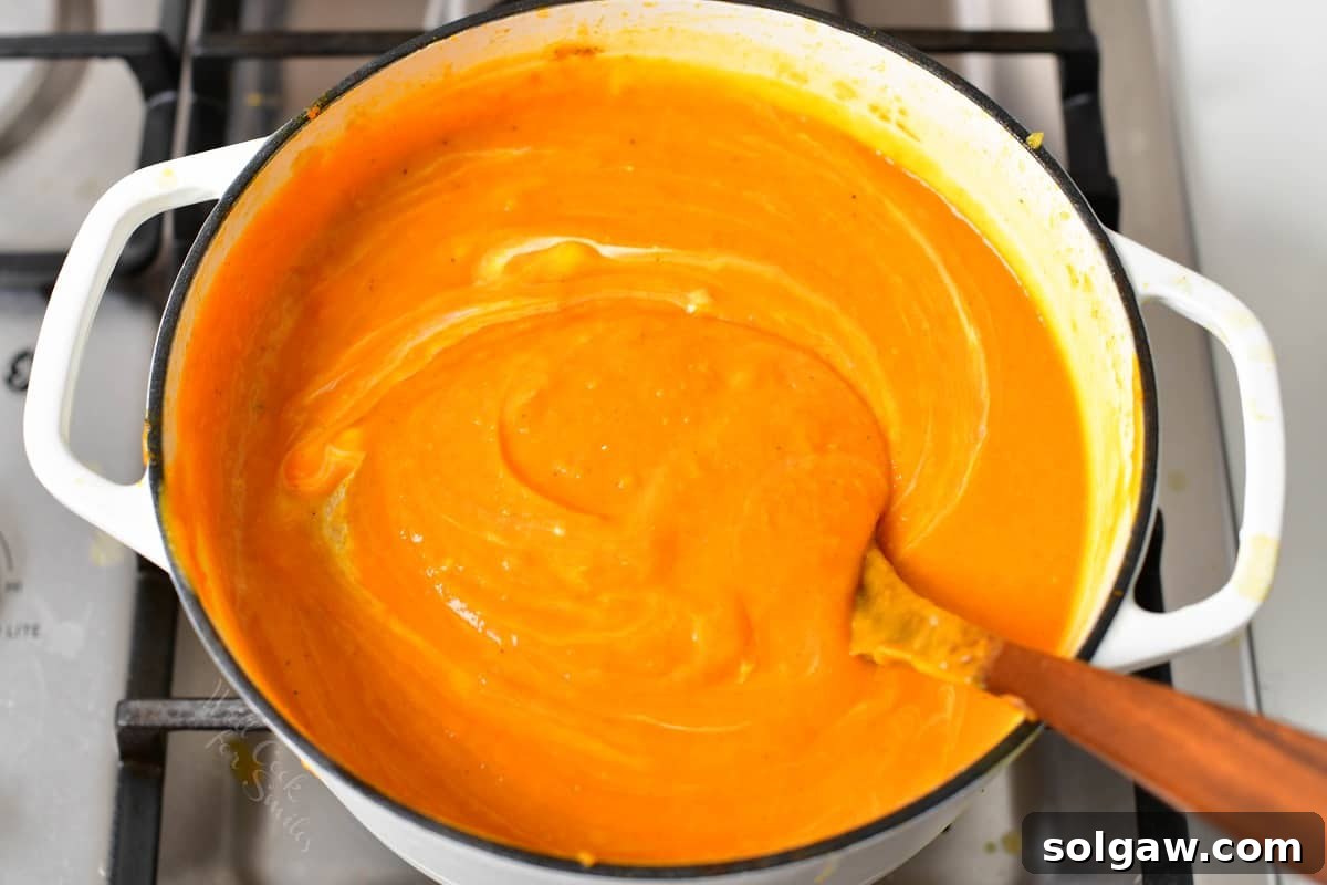 Heavy whipping cream being stirred into the smooth sweet potato soup in a pot with a wooden spoon.
