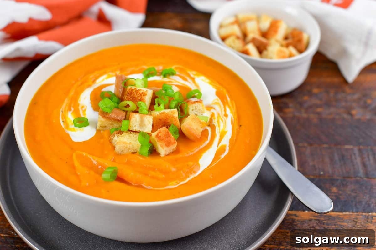 A bowl of sweet potato soup topped with crunchy croutons, with more croutons scattered next to the bowl.