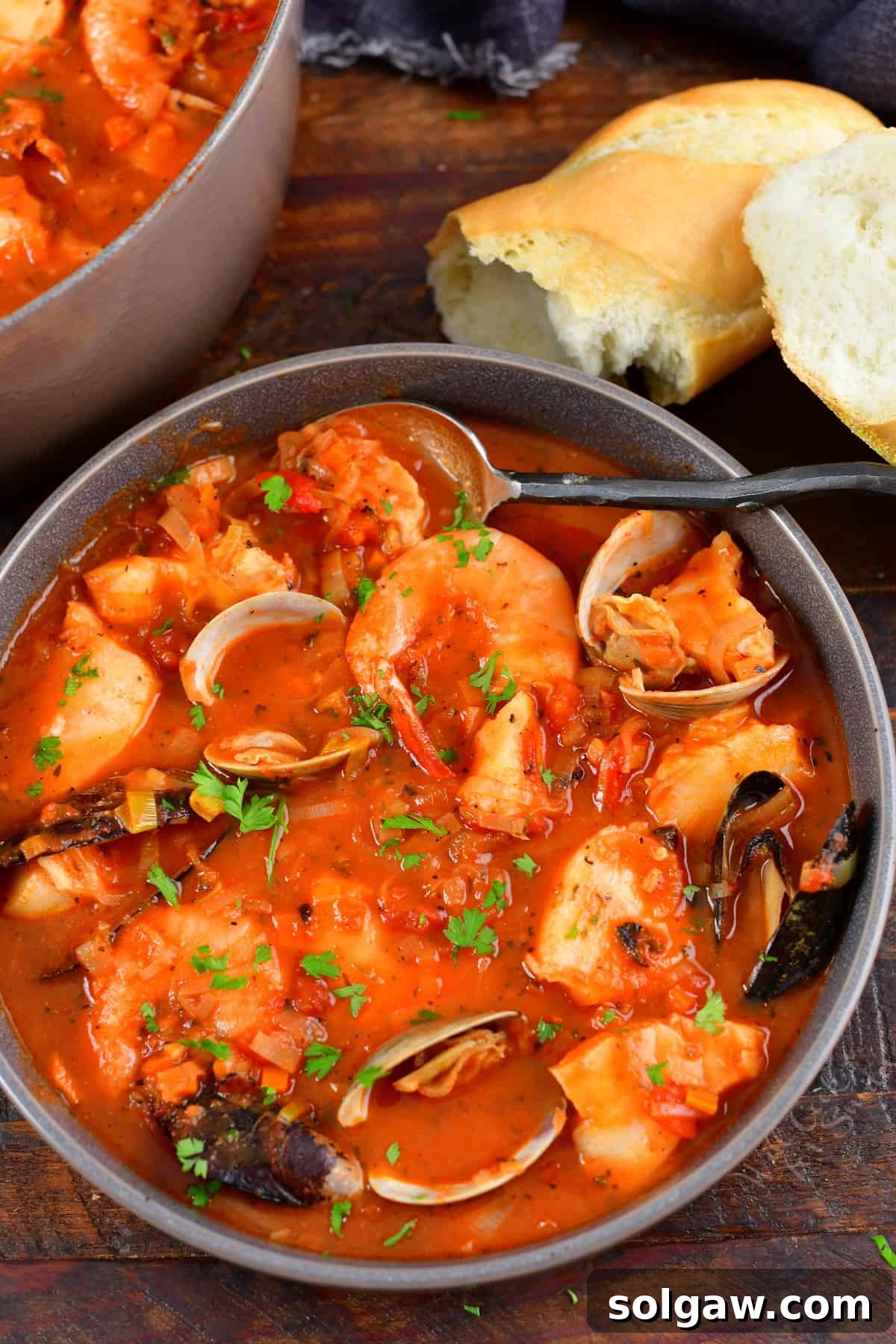 top view of Cioppino fish stew in a grey bowl with bread and a spoon