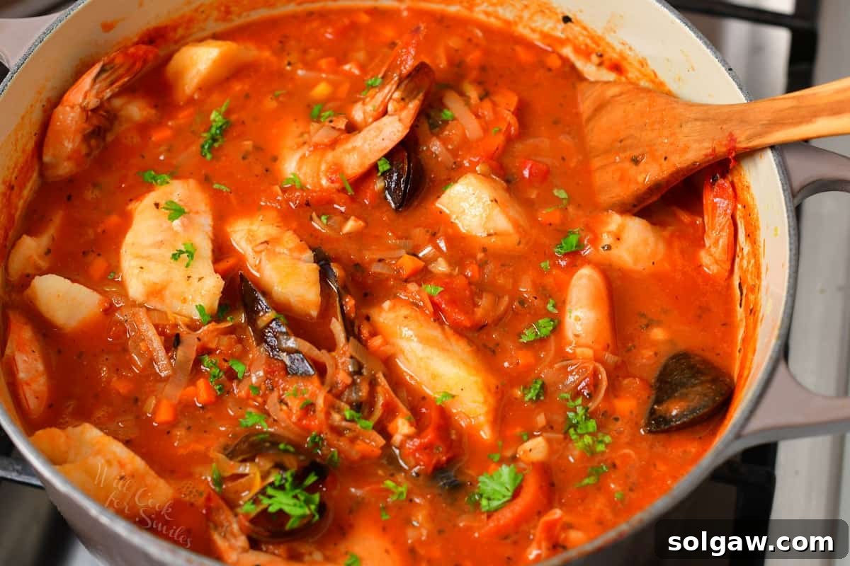 cooked Cioppino (seafood stew) in a pot on the stove with a wooden spoon.