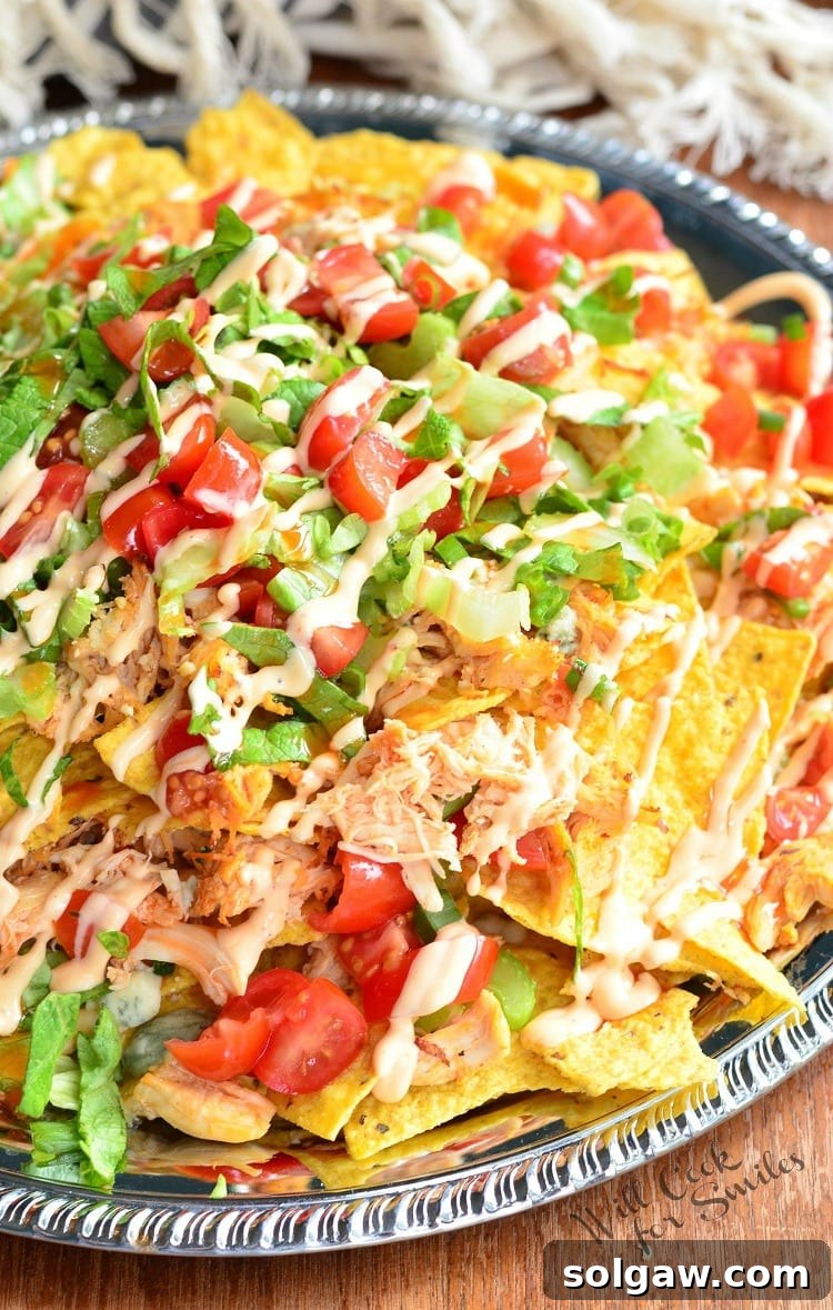 Buffalo Chicken Nachos on a metal serving platter on a table, garnished with fresh herbs