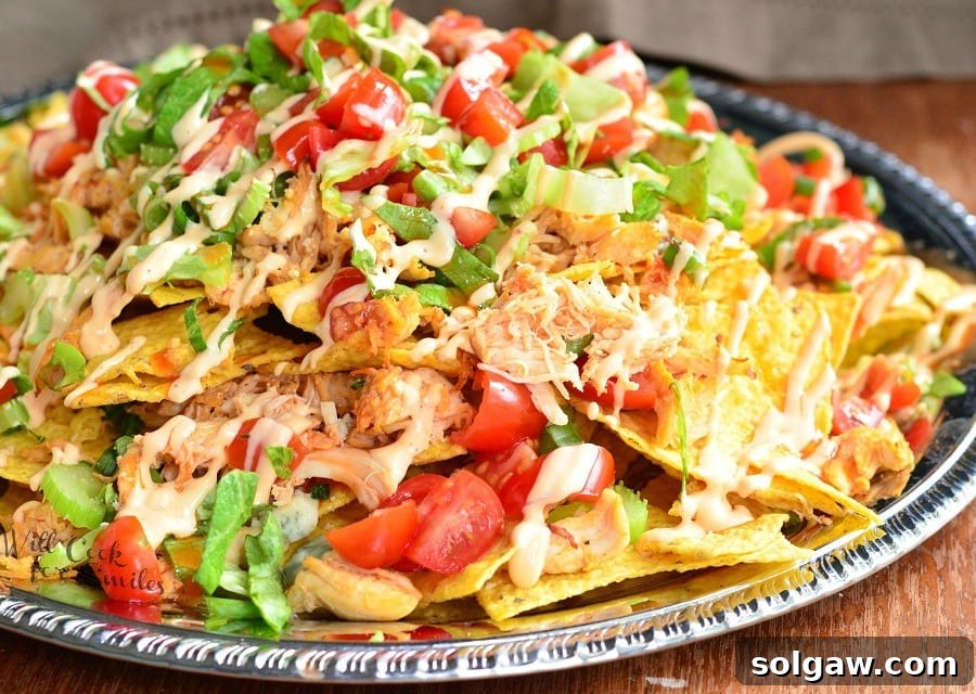Horizontal shot of Buffalo Chicken Nachos on a metal serving platter on a table, with a hand reaching for a chip