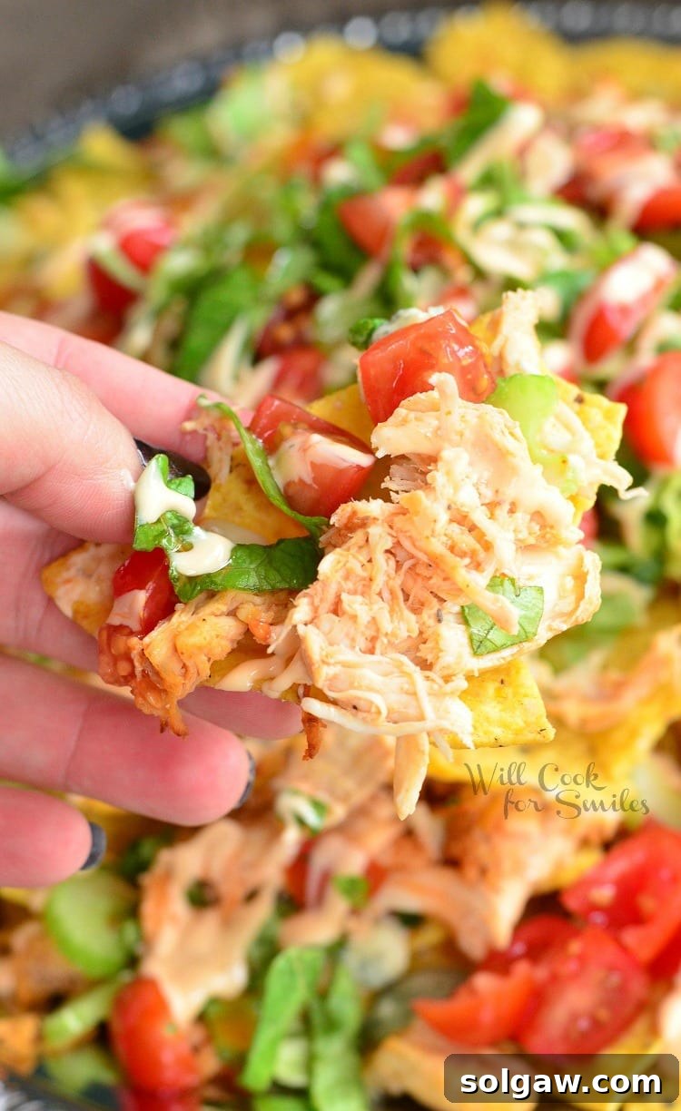 Holding a nacho with Buffalo Chicken Nachos on a metal serving platter in the background, showing the layers