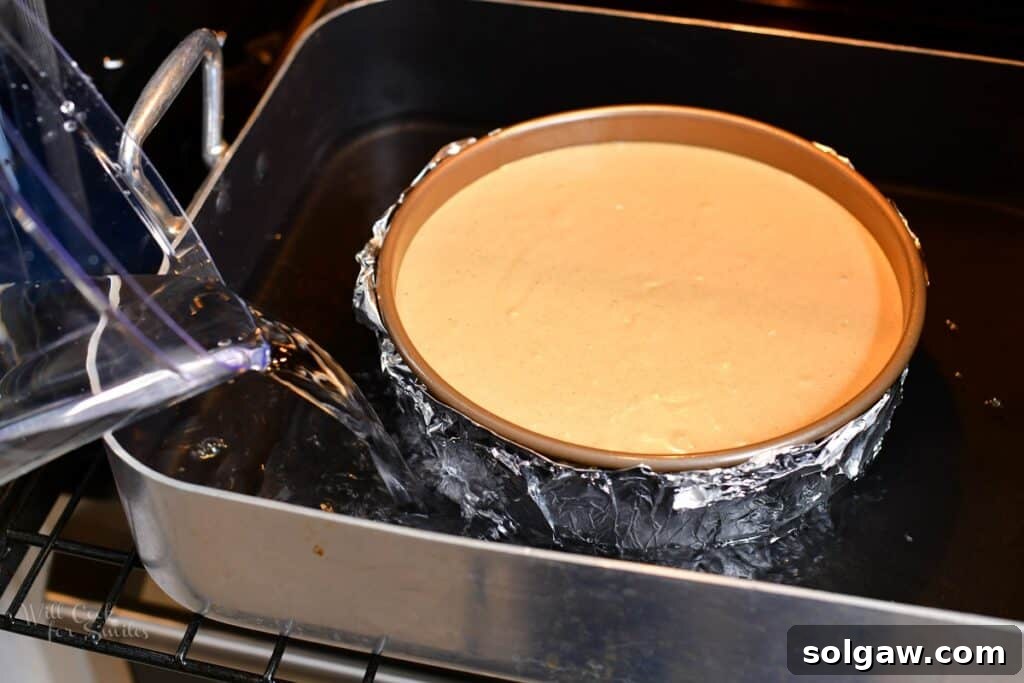The process of pouring hot water into the roasting pan to create a water bath around the cheesecake springform, ensuring even baking and preventing cracks.