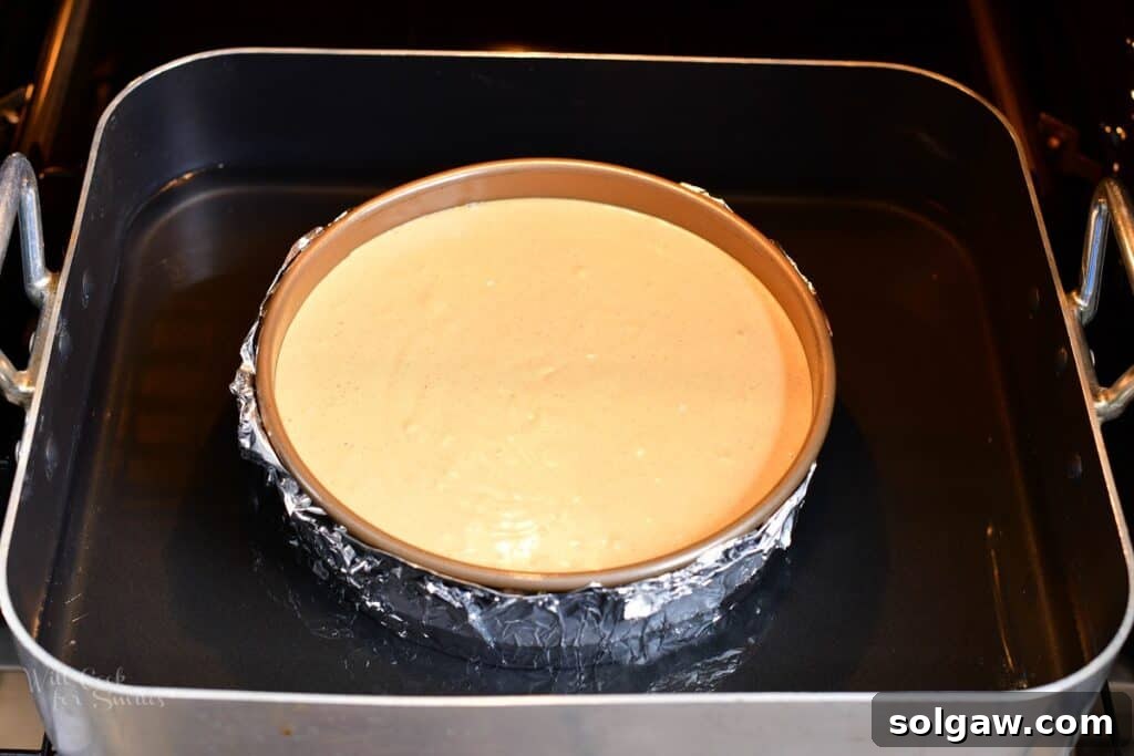 The cheesecake pan securely placed in a larger roasting pan, surrounded by hot water for a water bath, ready to be transferred to the oven for baking.