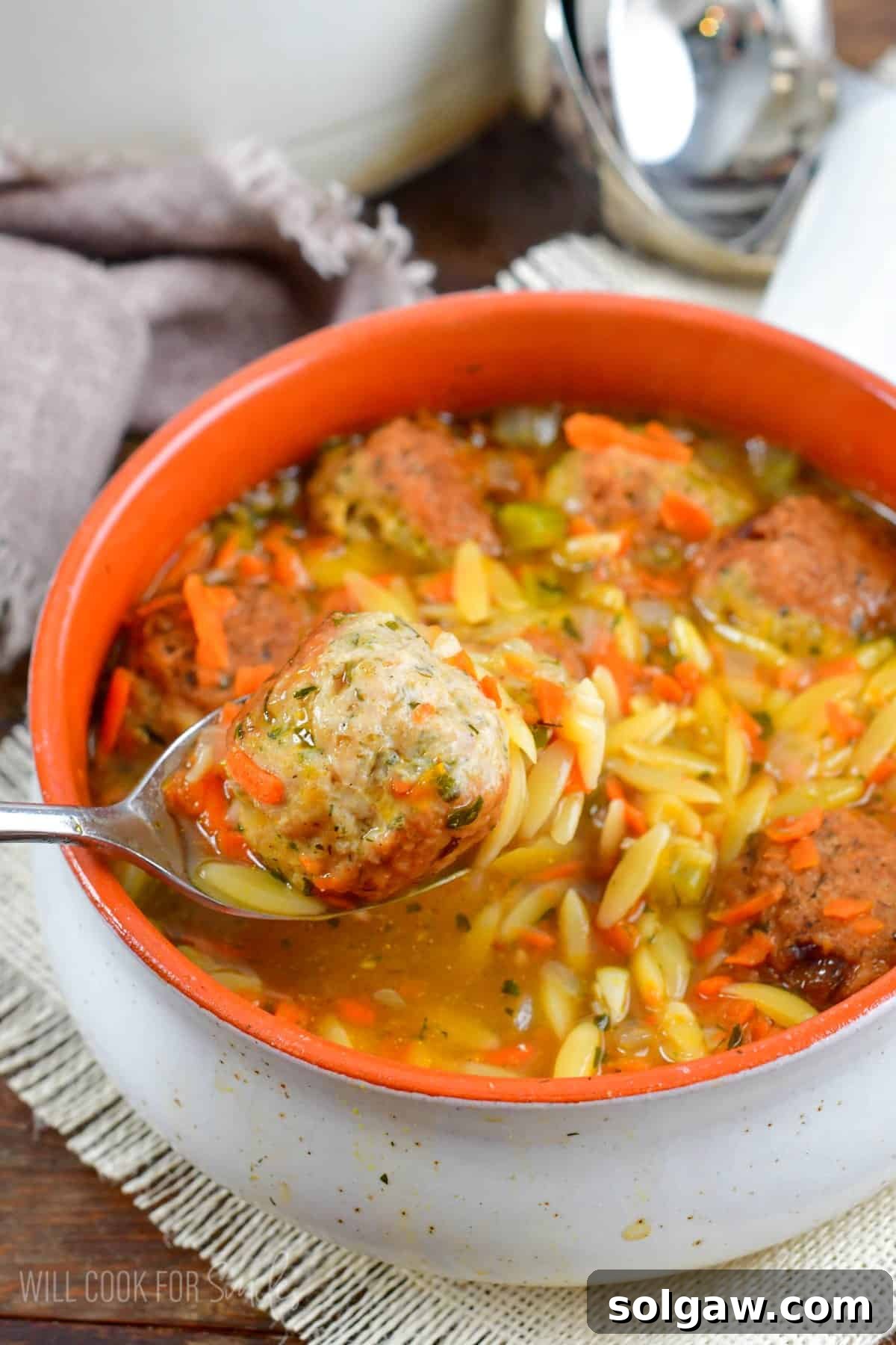 A spoon scooping a delicious chicken meatball from a hearty bowl of orzo soup, showcasing the tender meatball and perfectly cooked pasta.