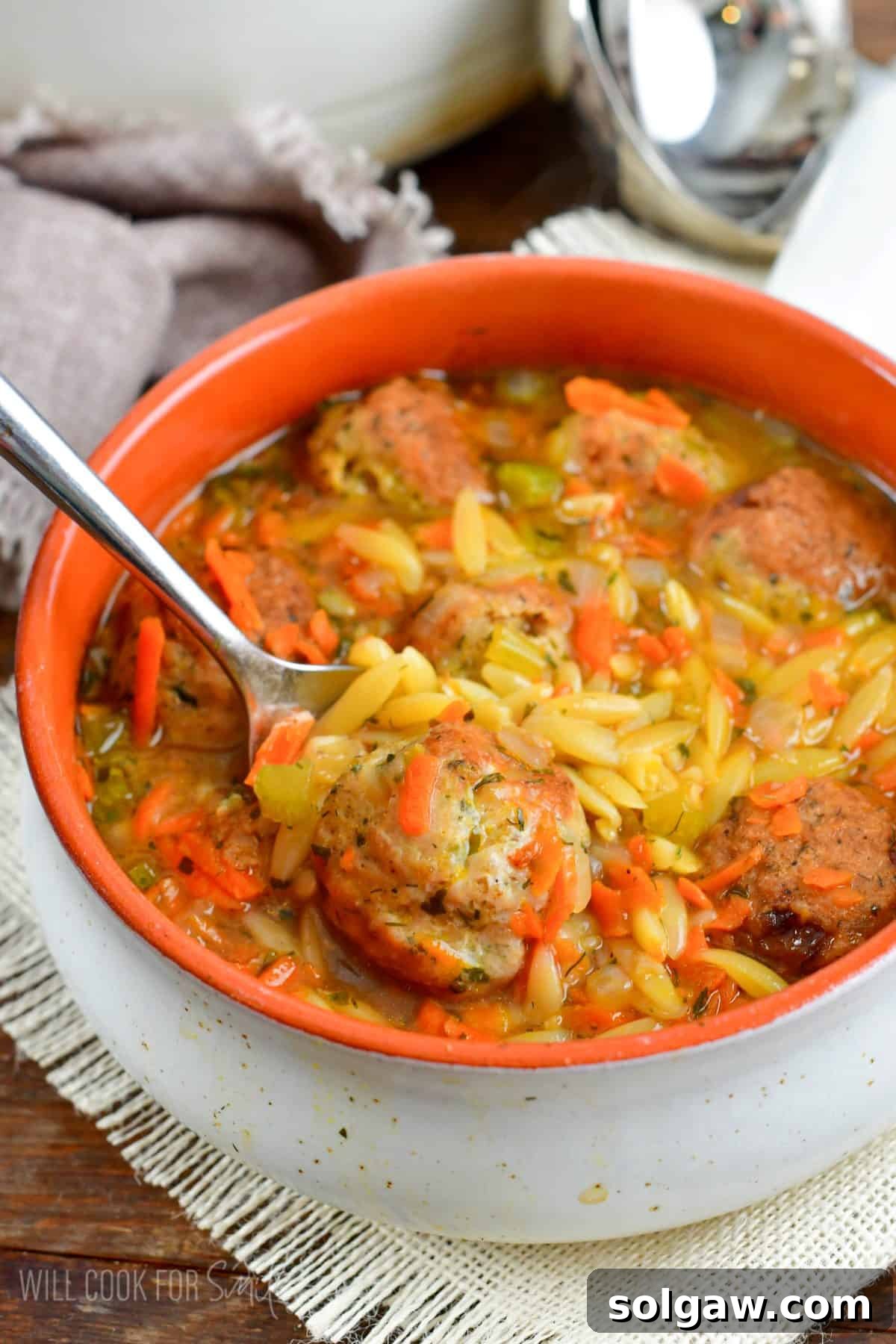 A close-up view of Chicken Meatball and Orzo Soup in a bowl, with a spoon poised to scoop, emphasizing its hearty and comforting appeal.