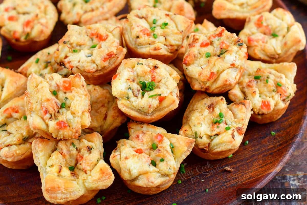 A close-up shot of several perfectly baked crab puffs, stacked artfully on a white plate, highlighting their golden brown pastry and creamy filling.