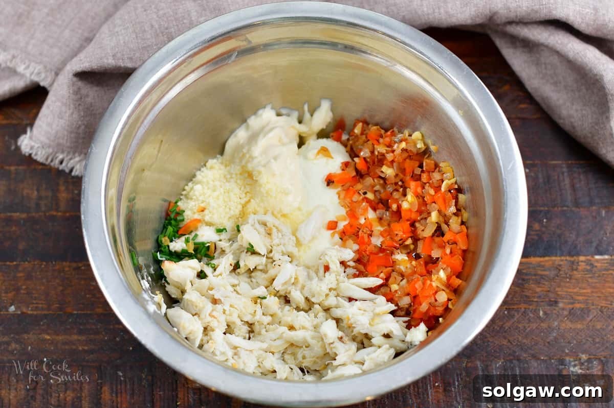 A bowl filled with finely diced onions, red bell peppers, and minced garlic, illustrating the prepared vegetable base for the crab filling.