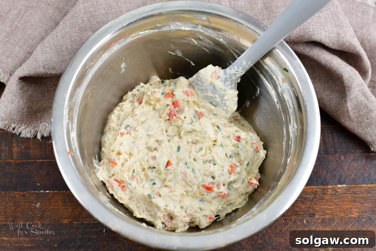 A mixing bowl with all the creamy crab puff filling ingredients thoroughly combined, including lump crab meat, cream cheese, parmesan, and sautéed vegetables.