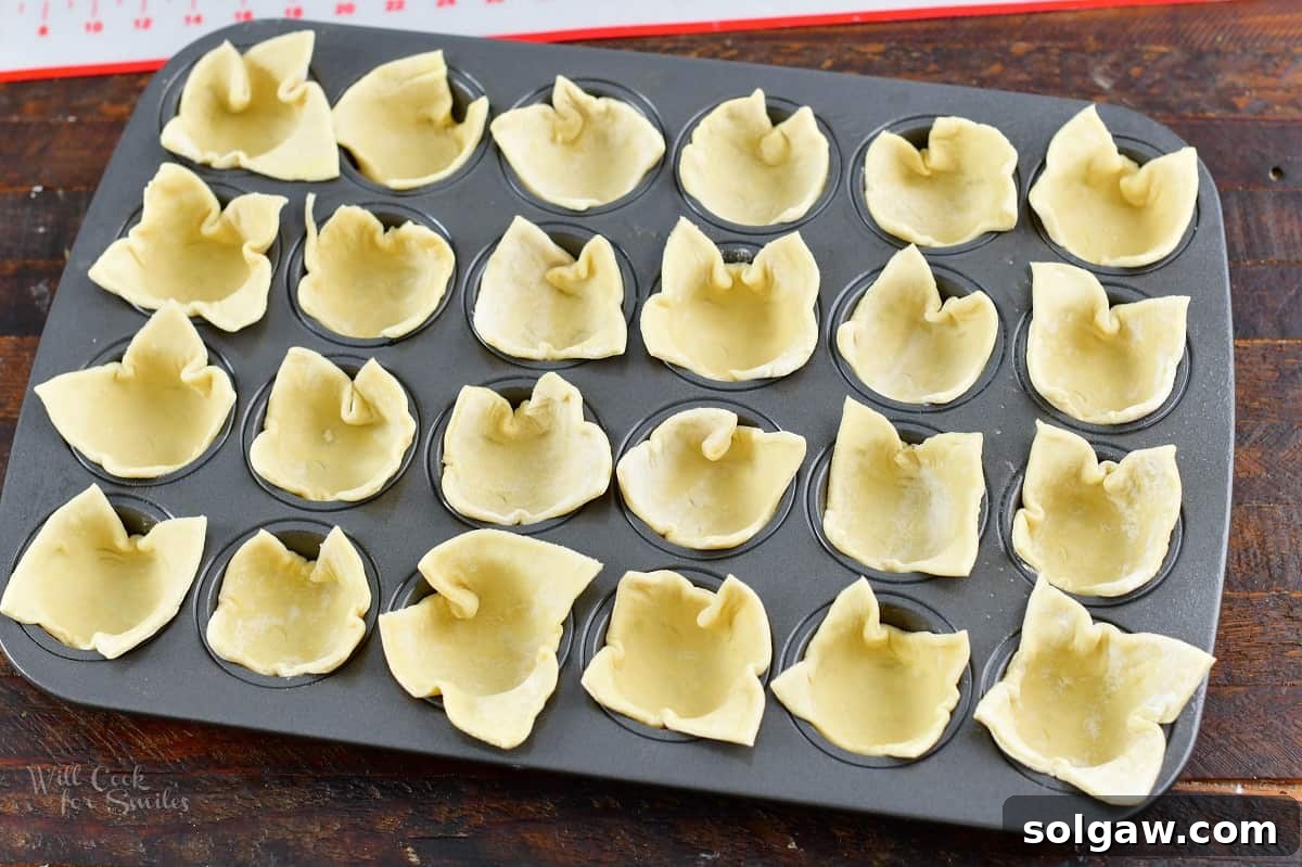 Mini muffin tin with puff pastry squares carefully pressed into each cup, forming the base for the crab puffs.