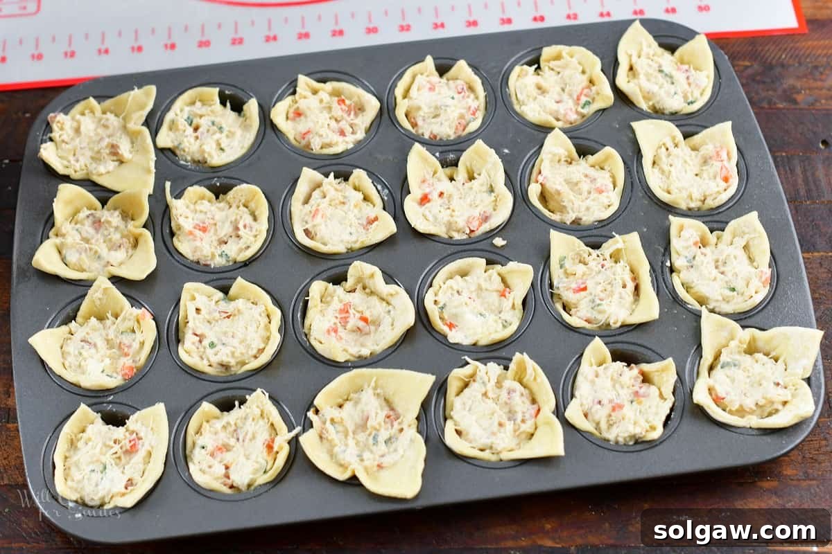 Mini muffin pan with all puff pastry cups filled with the creamy crab mixture, ready for baking.