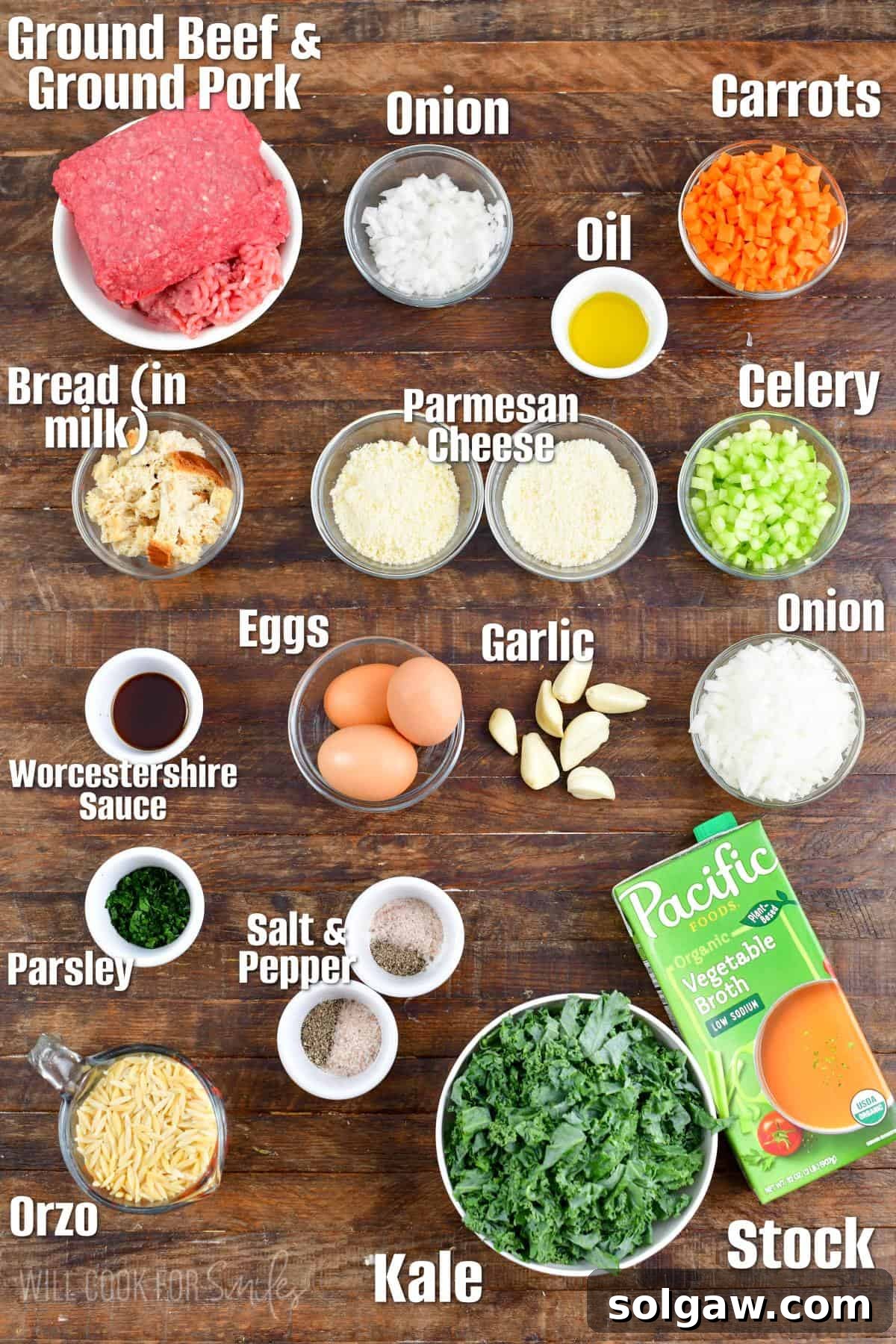 Neatly arranged key ingredients for Italian wedding soup, including ground meats, eggs, cheese, vegetables, and small pasta, on a wooden cutting board.