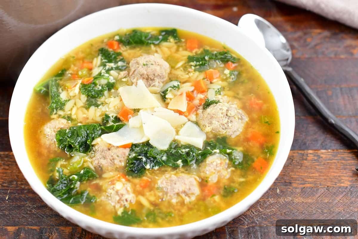 A close-up of a steaming bowl of Italian Wedding Soup, garnished with freshly shaved Parmesan cheese, highlighting its comforting appeal.