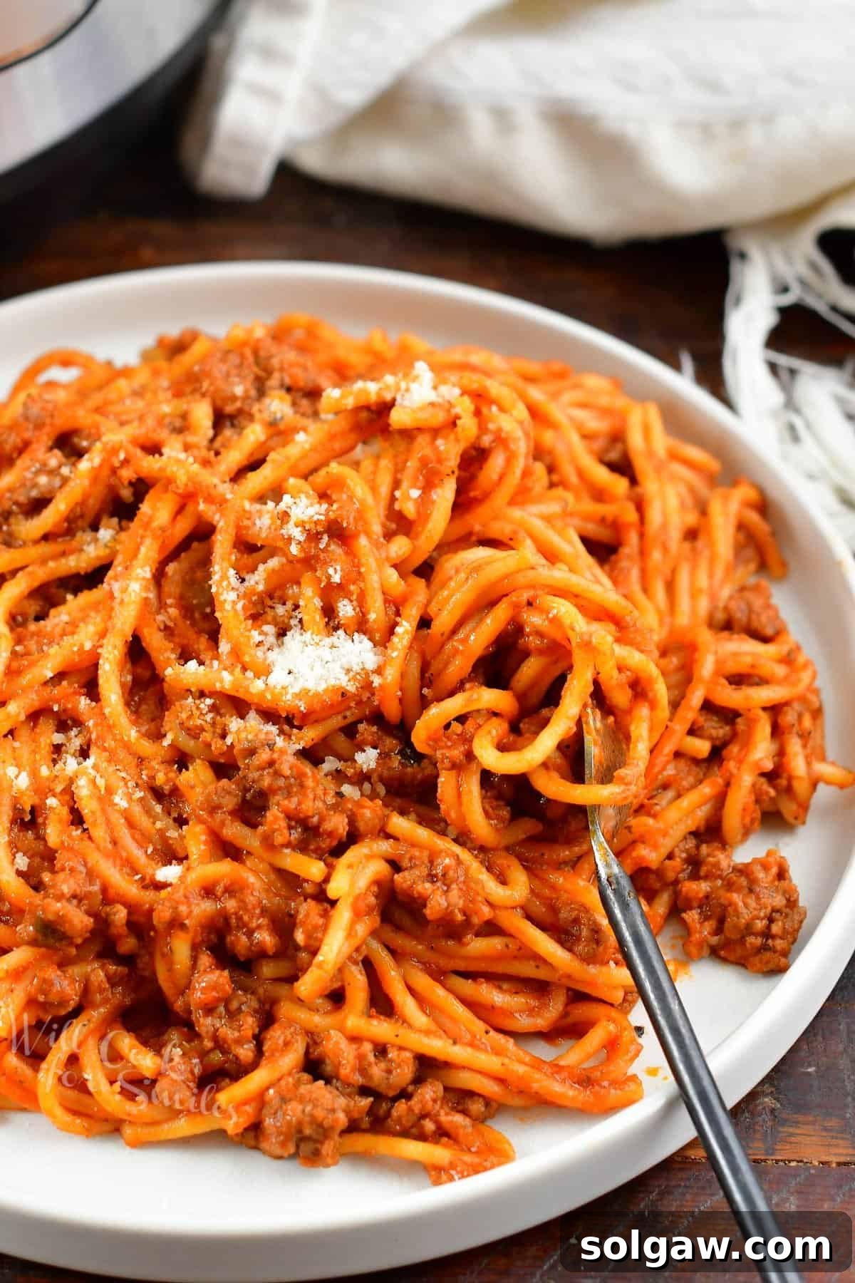 Swirling tender Instant Pot spaghetti with rich meat sauce onto a fork on a plate, garnished with fresh herbs and grated Parmesan.