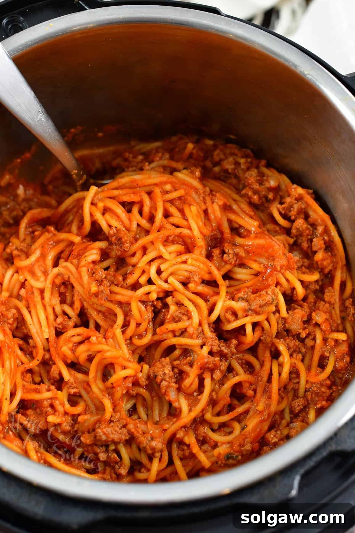 Scooping a generous portion of Instant Pot spaghetti with rich meat sauce directly from the pot into a serving bowl.