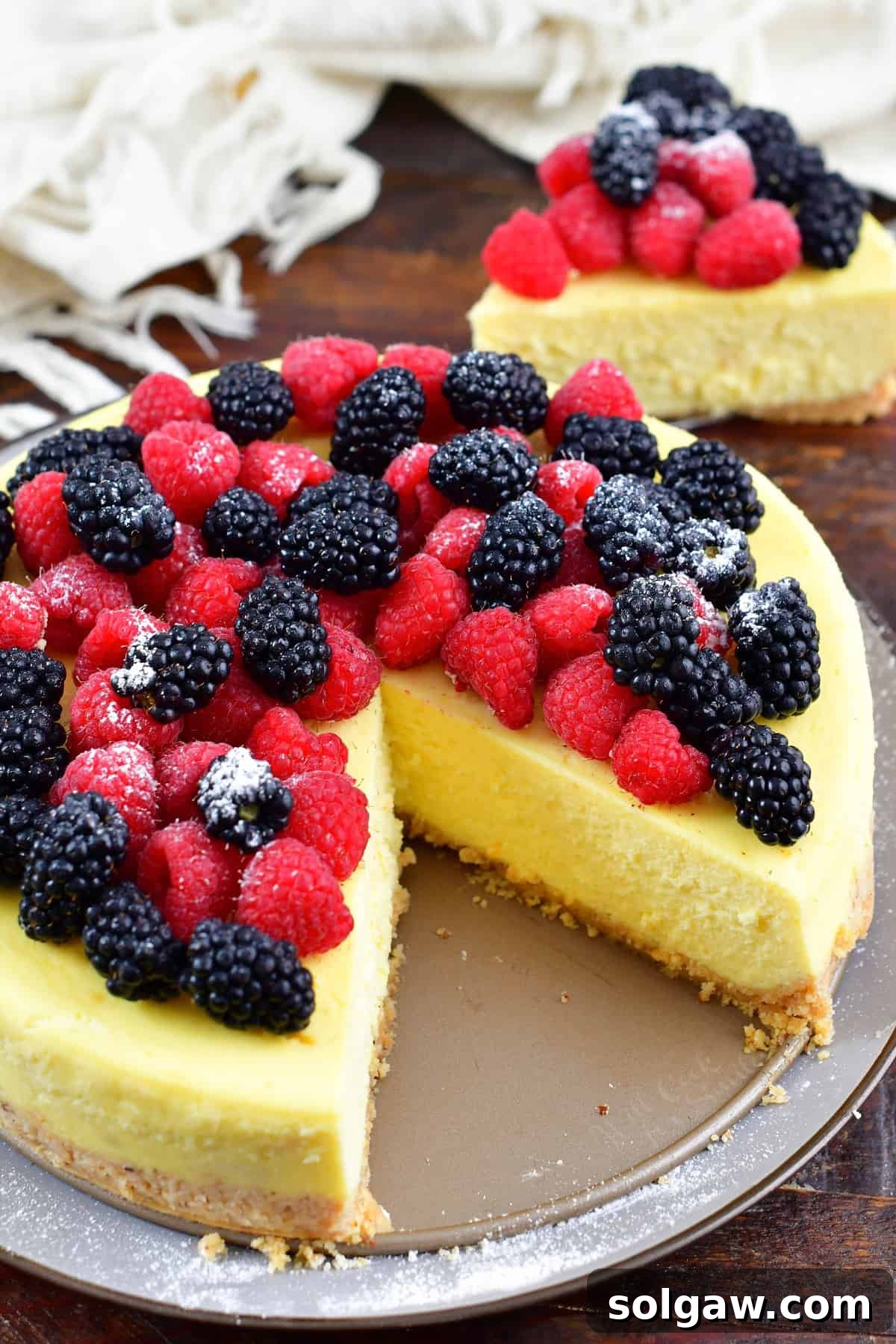 Top-down view of a whole ricotta cheesecake with a slice neatly cut out, garnished with fresh berries.