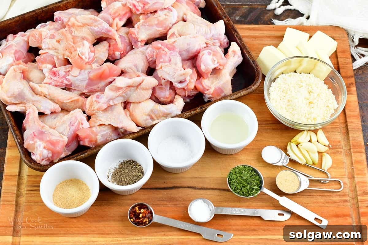 Crispy Air Fryer Garlic Parmesan Wings 3 Ingredients for air fryer chicken wings laid out on a cutting board, including fresh garlic, butter, parmesan cheese, and raw chicken wings.