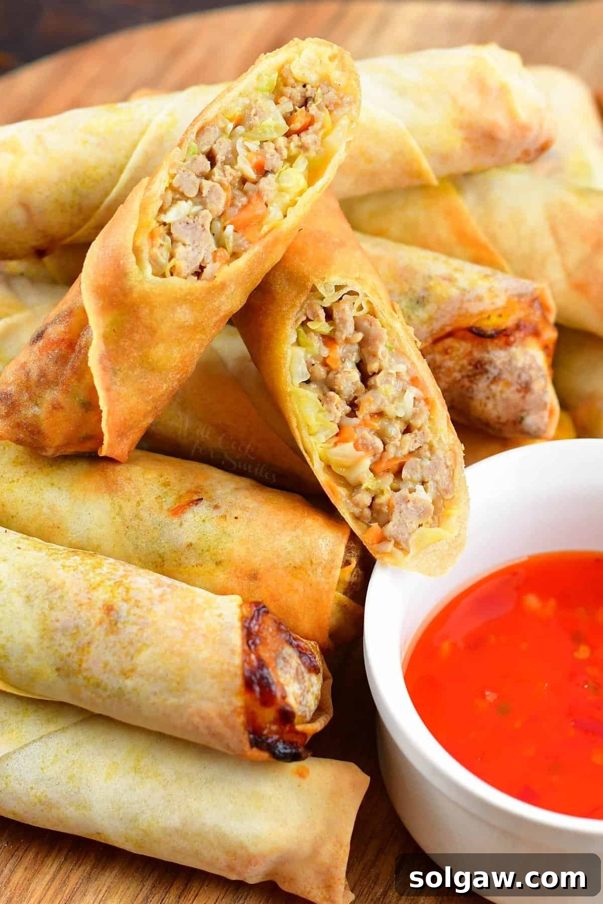 Two halves of a perfectly fried Thai spring roll, stacked on top of more golden-brown spring rolls. The wrapper is thin and crispy, revealing a hearty, flavorful filling.