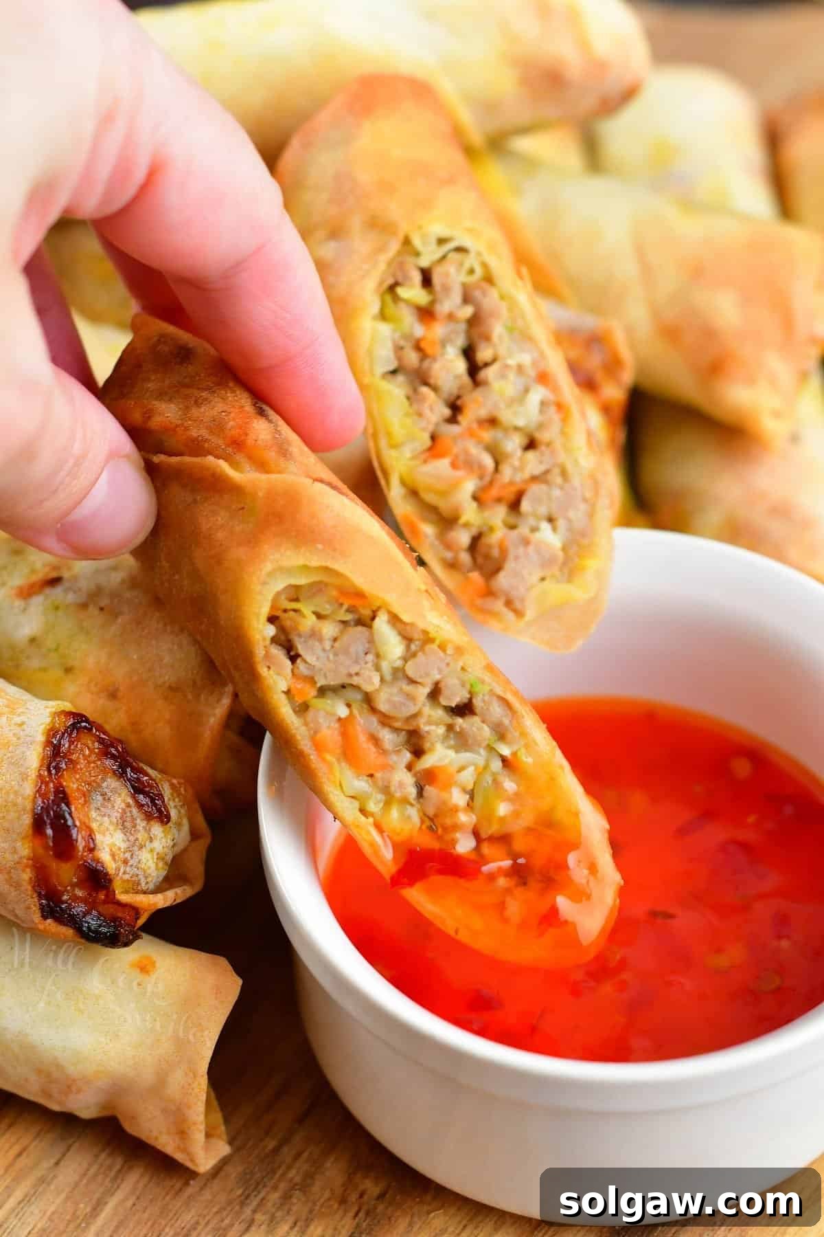 A perfectly cooked Thai spring roll half being dipped into a luscious sweet Thai chili sauce, highlighting its crispy exterior.