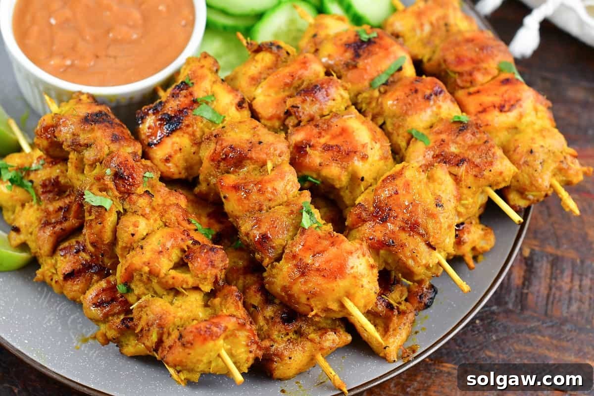Sizzling Thai Chicken Satay with Velvety Peanut Sauce 5 A plate of grilled Thai Chicken Satay skewers with a side of creamy peanut sauce, garnished with fresh herbs and lime wedges.