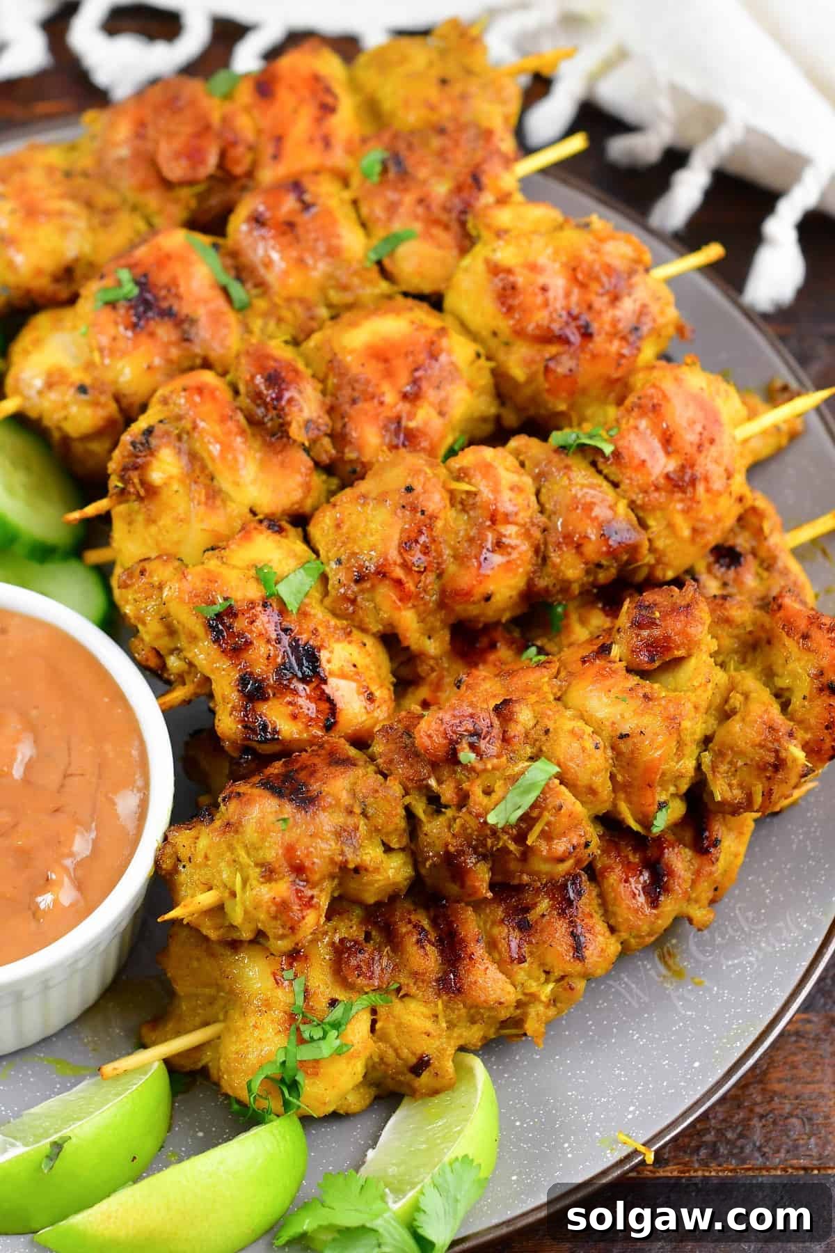 Sizzling Thai Chicken Satay with Velvety Peanut Sauce 6 Multiple skewers of golden-brown Thai Chicken Satay, layered attractively on a white serving plate, ready to be enjoyed.