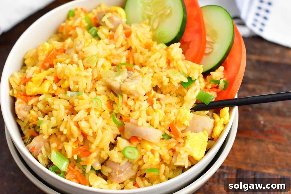 Side view of Thai fried rice in a bowl with cucumber and tomato slices, garnished with fresh herbs.