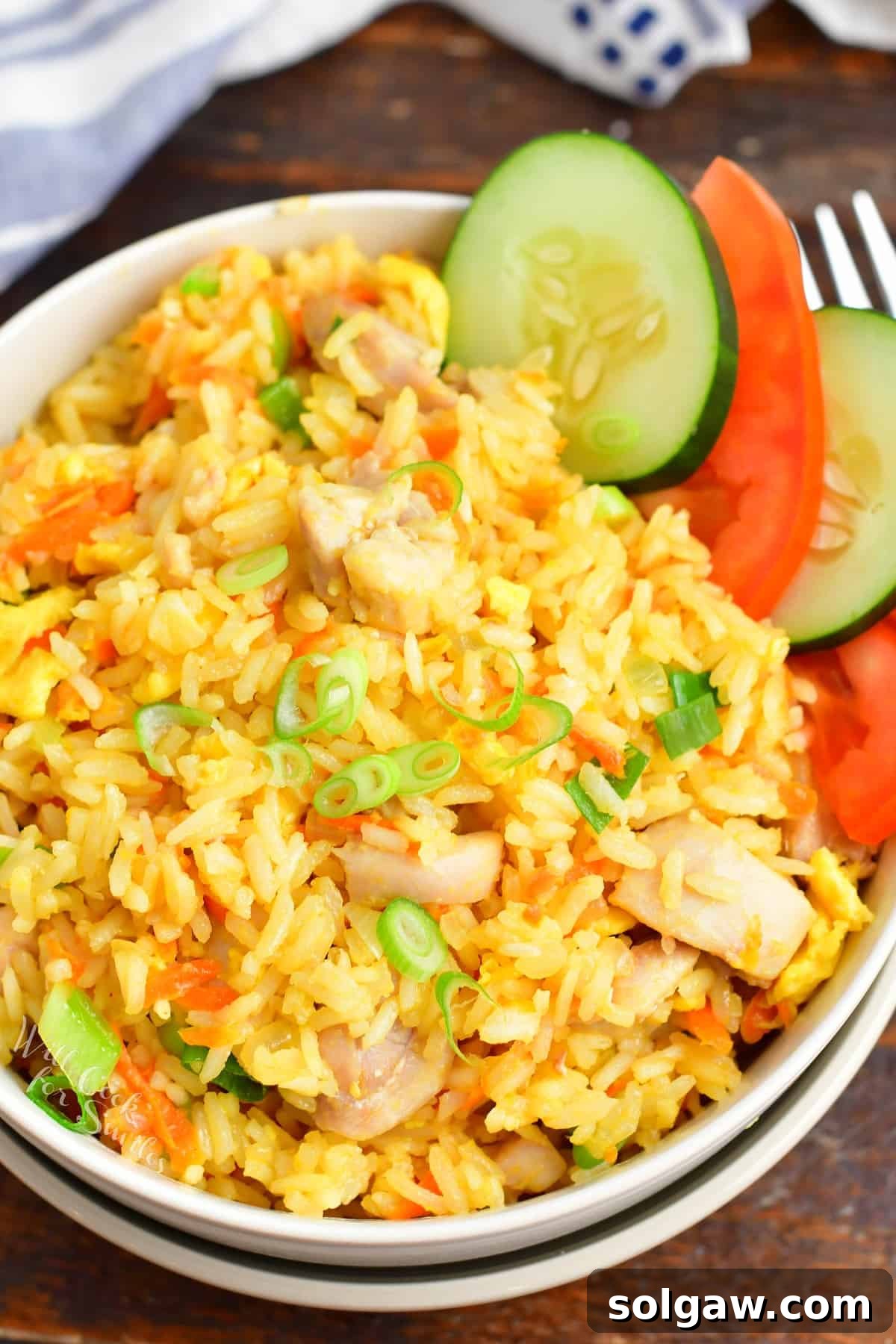 Top view of Thai fried rice served in a bowl, garnished with cucumber and tomato slices, ready to eat.