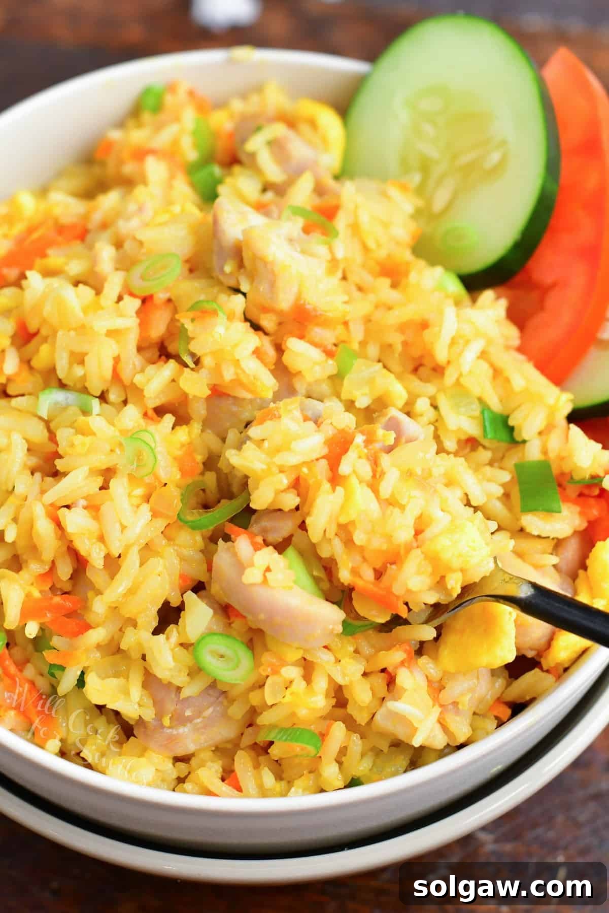Close up and scooping Thai fried rice in a bowl with cucumber and tomato slices